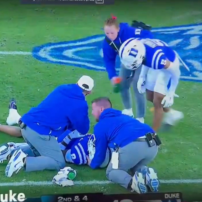 Football player receiving treatment as woman in blue approaches on football field