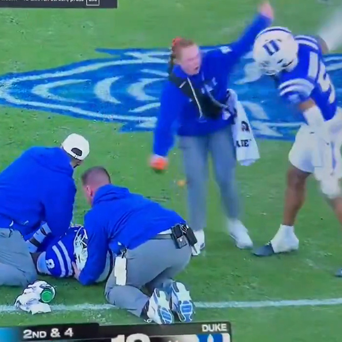 Woman in blue approaching football player receiving treatment on field