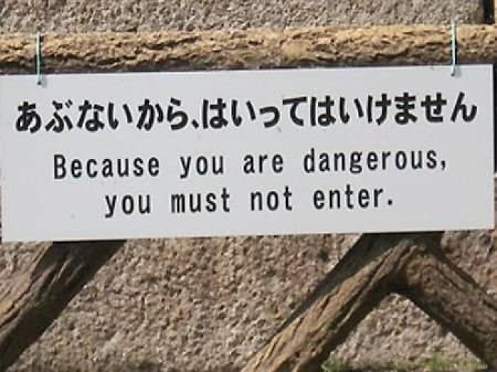 A sign on a wooden fence displaying translation fails saying Because you are dangerous, you must not enter.