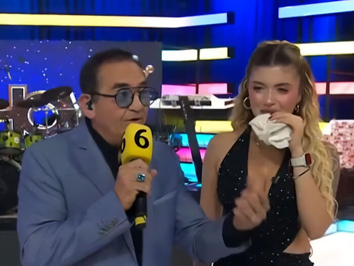 TV show host holding a microphone next to an injured model covering her face on set