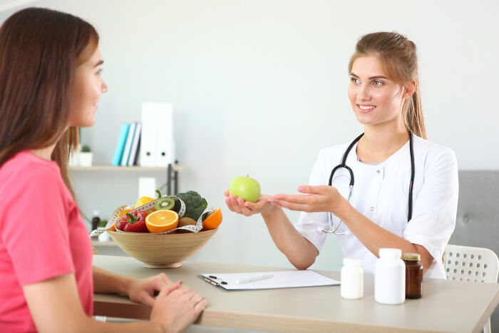 Nutritionist giving an apple to a patient, exchanging quick-fire jokes about healthy eating.