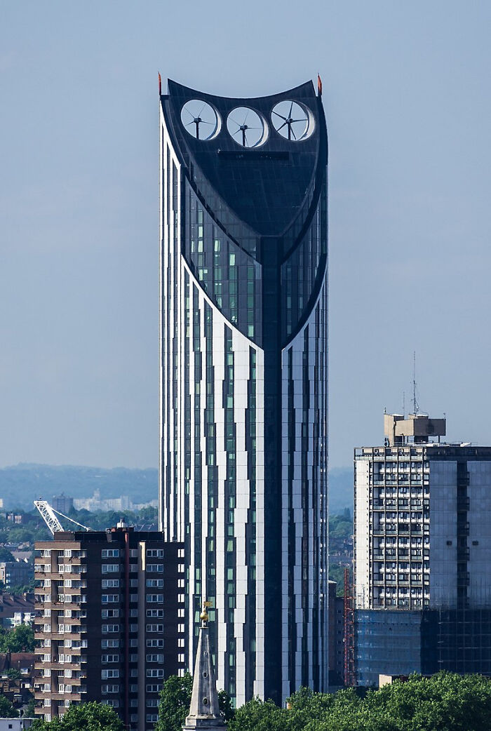 Tall strange building with three large circular wind turbines on top