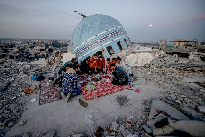 Group of people sharing meal on rubble near damaged mosque dome