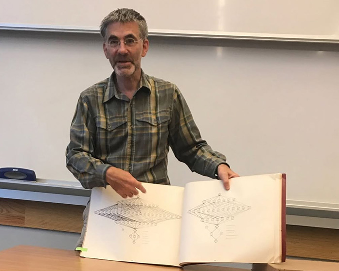 UC Berkeley professor standing in a classroom pointing to complex diagrams in a large book.