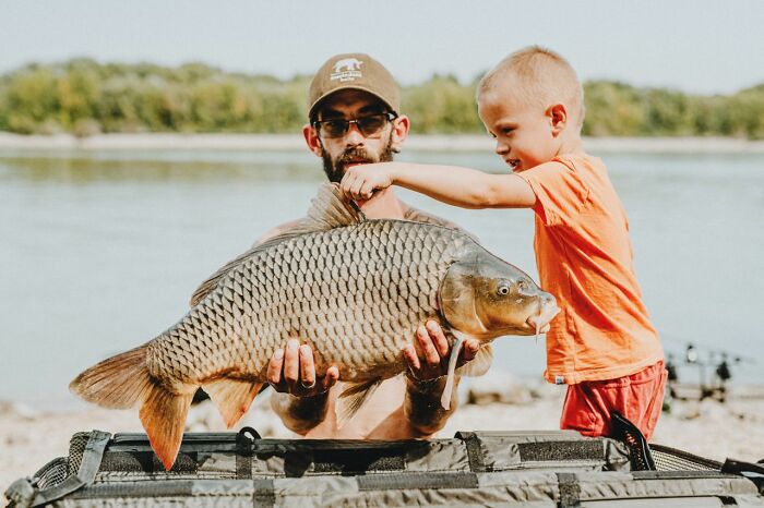 A man and a young boy holding a huge carp outdoors, sharing true stories of incredible fish catches.