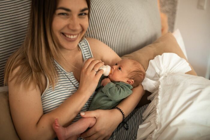 A smiling mother bottle feeding her newborn, sharing intimate true stories of family life.