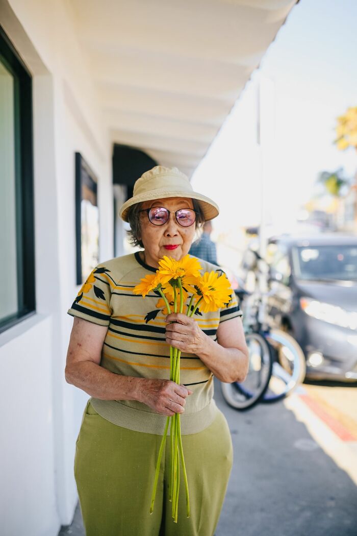 An elderly woman holding yellow flowers, sharing remarkable true stories people rarely tell.