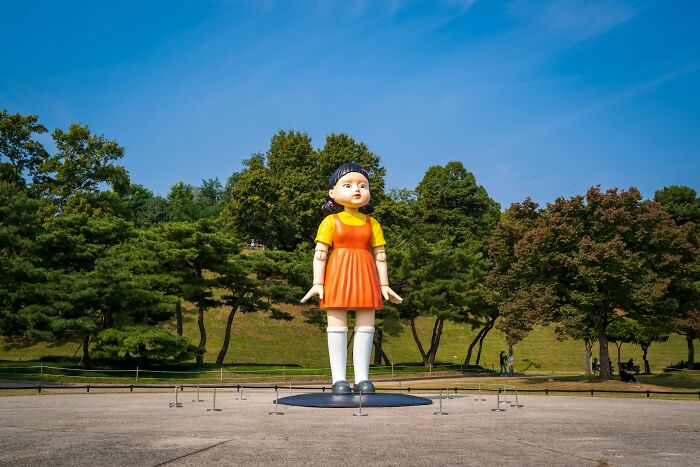 Giant Squid Game doll standing in a park, inspired by true stories.