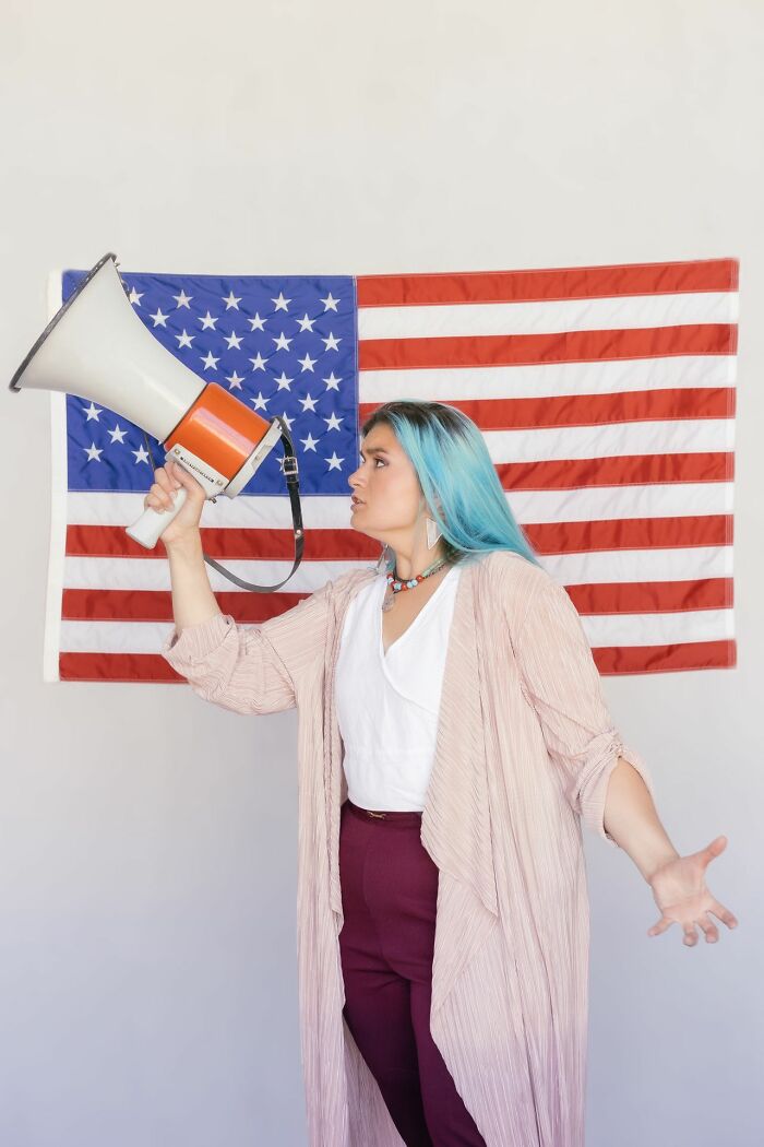 Woman with blue hair holding megaphone in front of American flag true stories concept