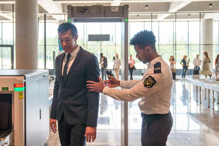 A security guard scans a man at airport security checkpoint, demonstrating unethical life pro tips for travel