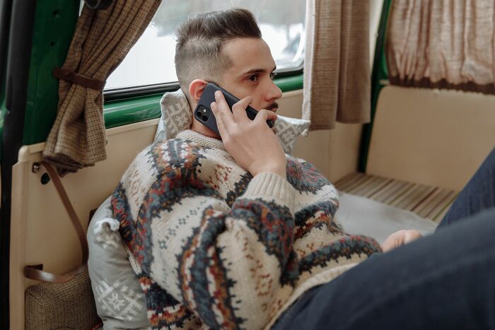A man sitting inside a camper van, holding a mobile phone to his ear. Unethical Life Pro Tips.