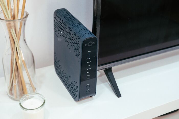 A black router sitting next to a television, representing unethical life pro tips for hacking wifi signals