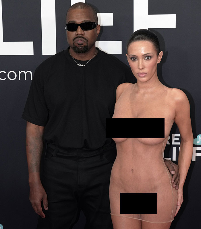 Kanye West and Bianca Censori posing together at an event with Censori in a sheer dress