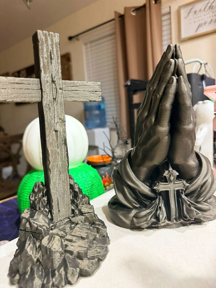 A detailed 3D printer creation of praying hands and a wooden-textured cross on a white surface.