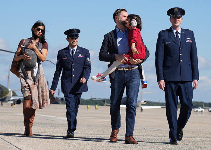JD Vance walks with Second Lady Usha Vance holding their child and military officers. JD Vance walks with Second Lady Usha Vance holding their child and military officers.