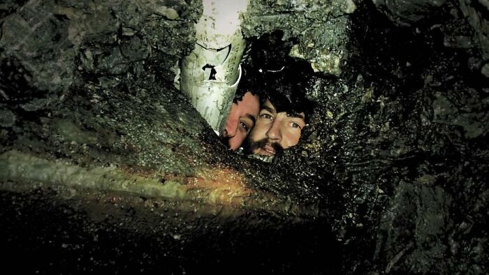 Two faces peering out from a dark hole under a pipe, showcasing entertaining pics.