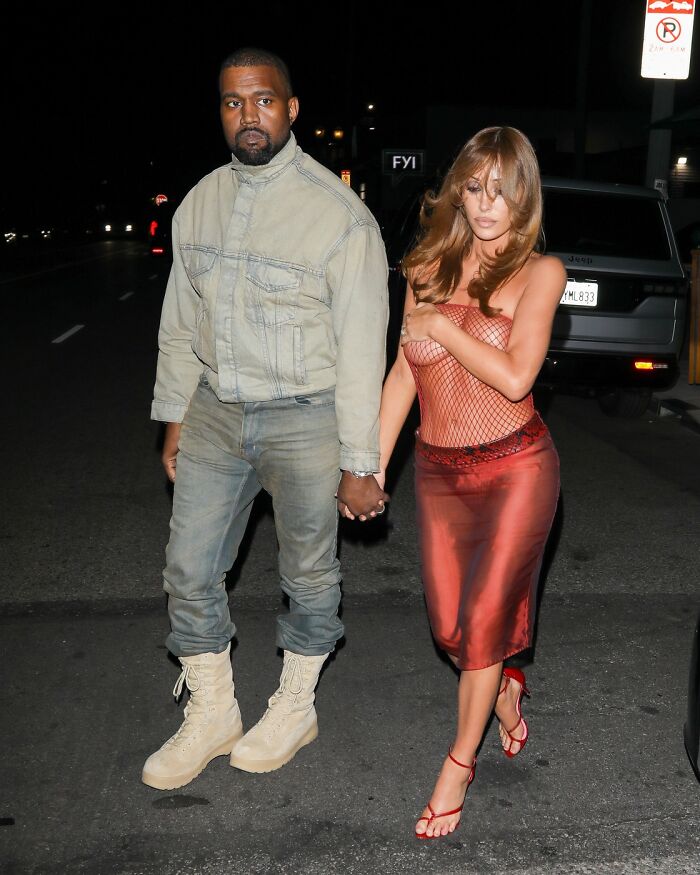 Kanye West holding hands with Bianca Censori wearing a sheer red fishnet outfit at night