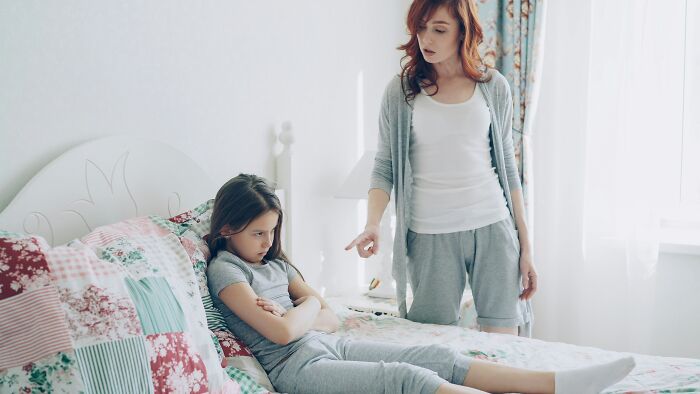 A mother gesturing sternly at her daughter in bed, illustrating dynamic with narcissistic parents.
