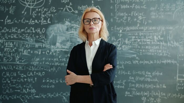 A stern-looking female teacher standing in front of a blackboard filled with complex math formulas.