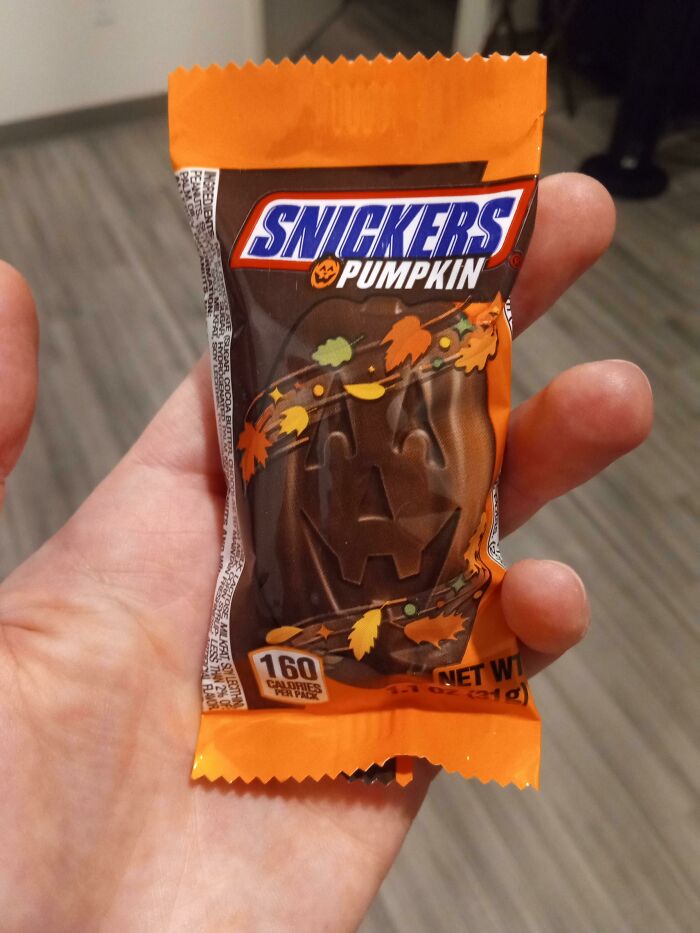 A hand holding a Snickers Pumpkin Halloween chocolate bar wrapped in orange foil