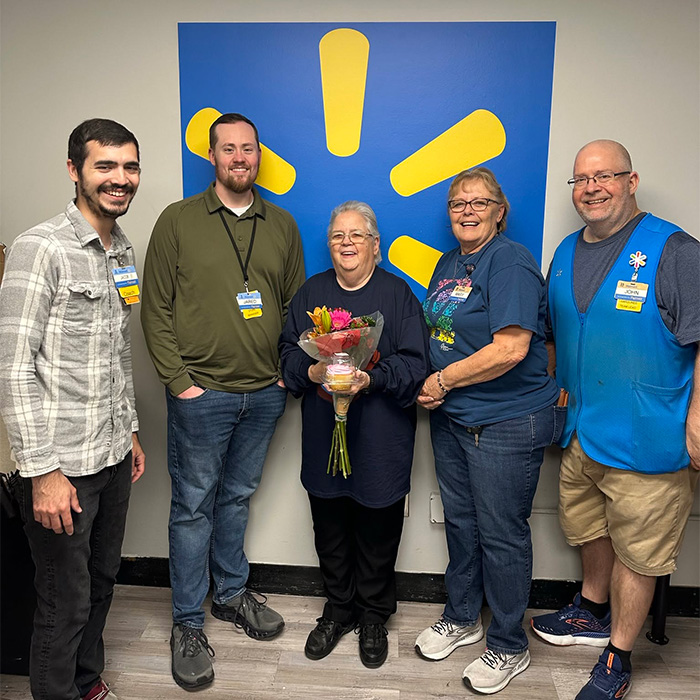 Walmart employee Gayle holding flowers surrounded by co-workers celebrating her retirement gift Walmart employee Gayle holding flowers surrounded by co-workers celebrating her retirement gift
