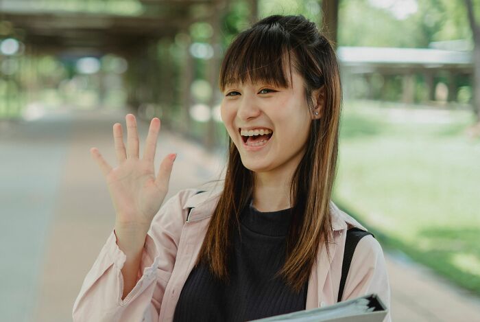 Smiling woman waving outdoors with greenery in background