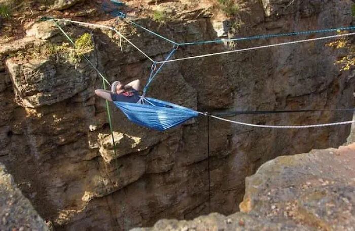 A person relaxing in a hammock suspended high above a steep canyon, fitting for cursed images.
