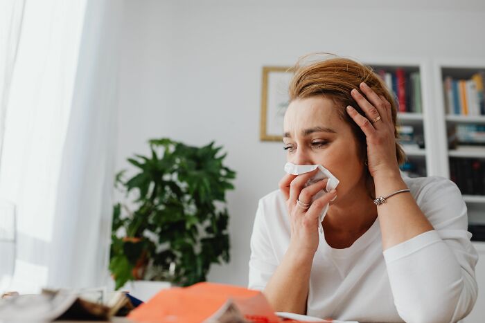 A woman blowing her nose with a tissue, illustrating human body facts about illness.