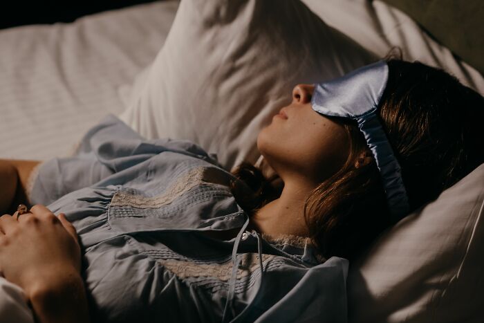 A woman sleeping in bed wearing an eye mask, representing human body facts about sleep.