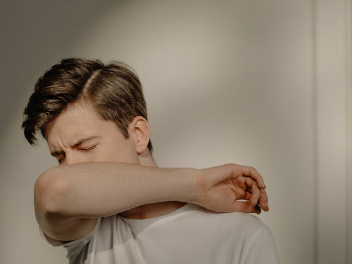 A young man sneezing into his elbow, illustrating human body facts related to reflexes.