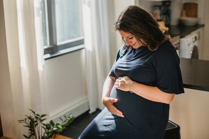 Pregnant woman holding her belly indoors demonstrating human body facts about pregnancy and growth.