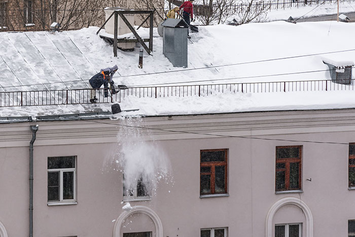 Worker removing snow from roof during winter job