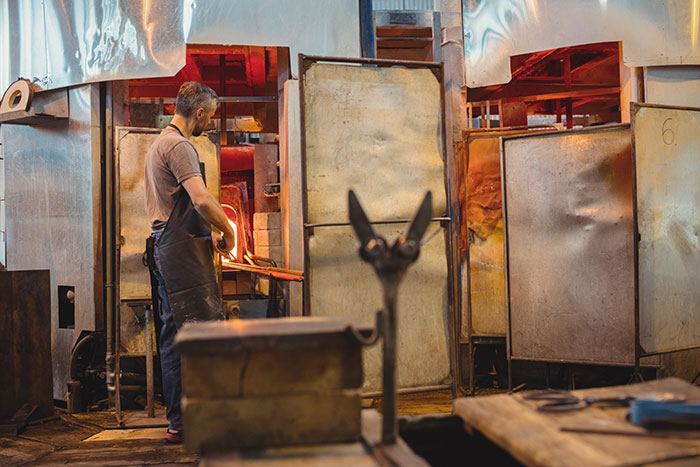 Worker handling molten glass in a high heat glassblowing factory job