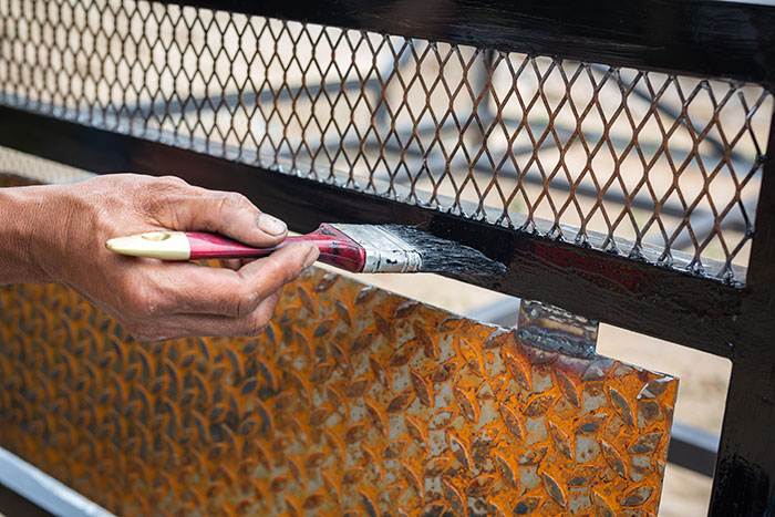 Painter applying black paint on metal fence in dangerous job