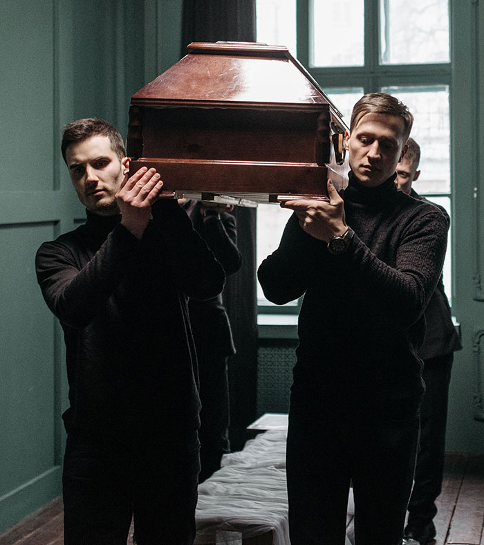 Pallbearers carrying coffin in a dimly lit room funeral job