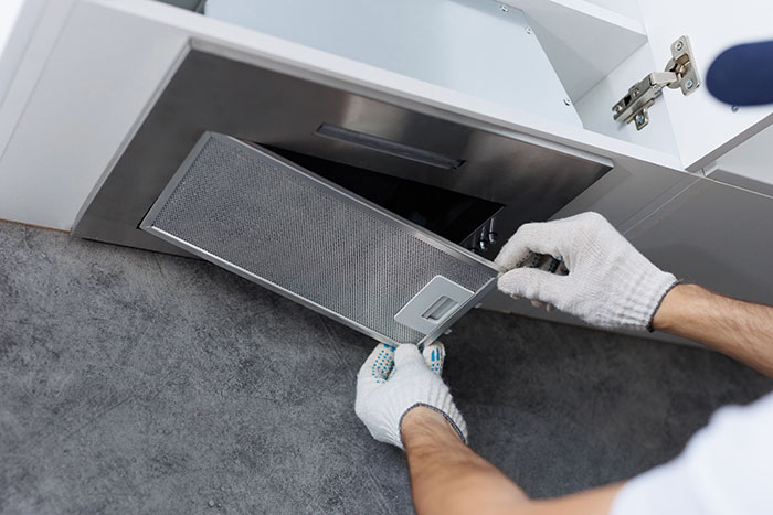 Worker installing a kitchen exhaust hood depicting hazardous jobs in appliance installation with good pay