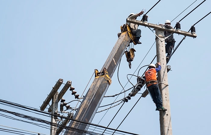 Electric linemen working on power lines atop utility pole