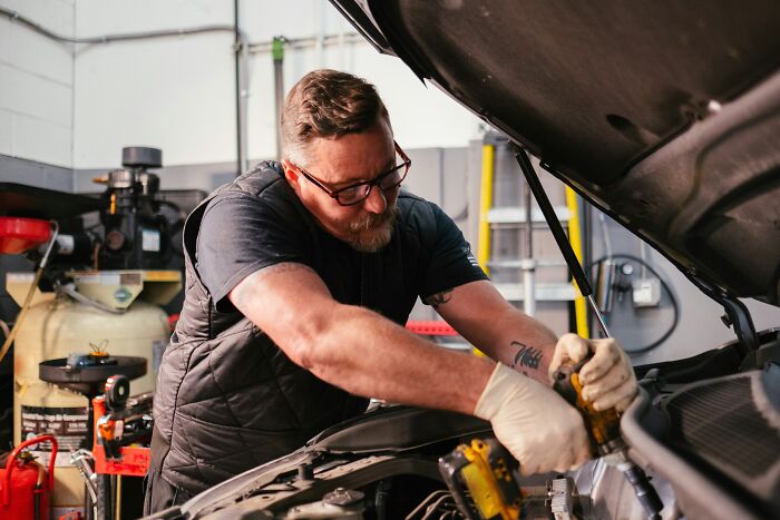 A mechanic fixing a car engine, acting as an industry insider in an auto shop.