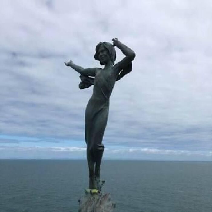A bronze statue of a woman overlooking the ocean, representing classical public art near the coast.