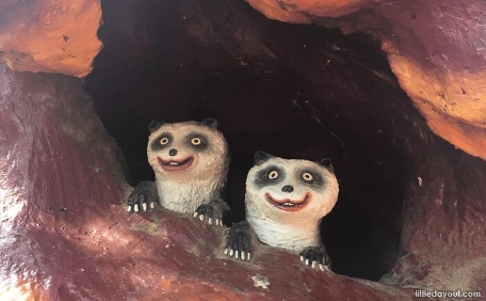 Hilarious and bizarre public art showing two creepy smiling panda statues peeking from a dark cave hole