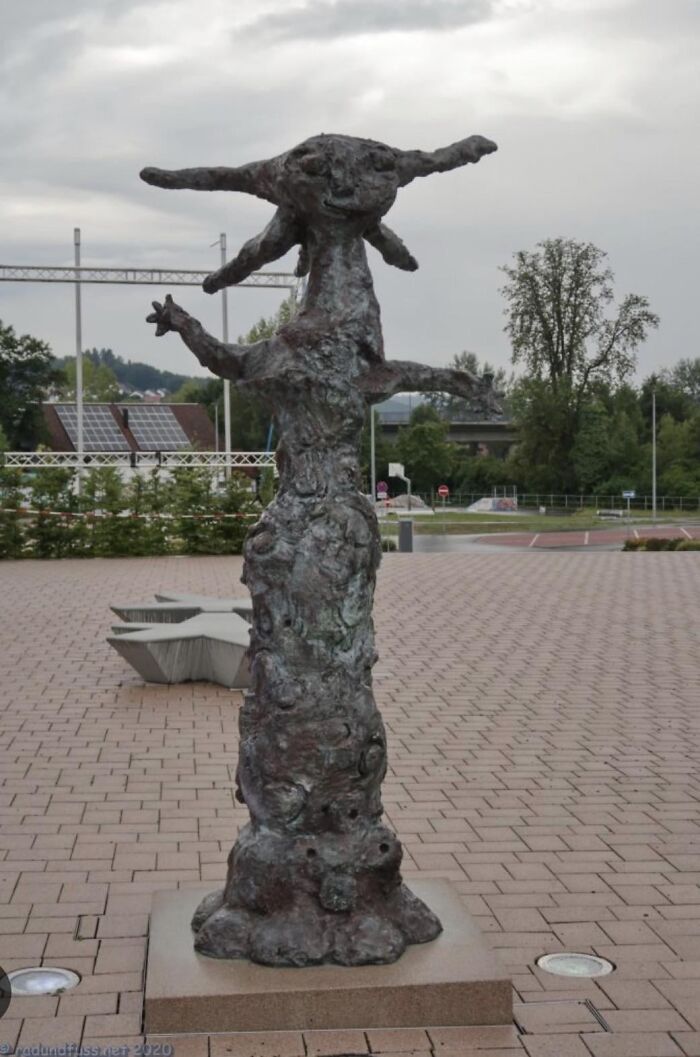 An abstract, rough-textured bronze sculpture in a paved plaza, showcasing a bizarre public art style.