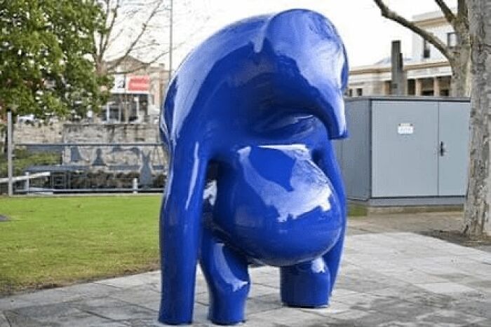 A shiny, abstract blue public art statue in a park setting