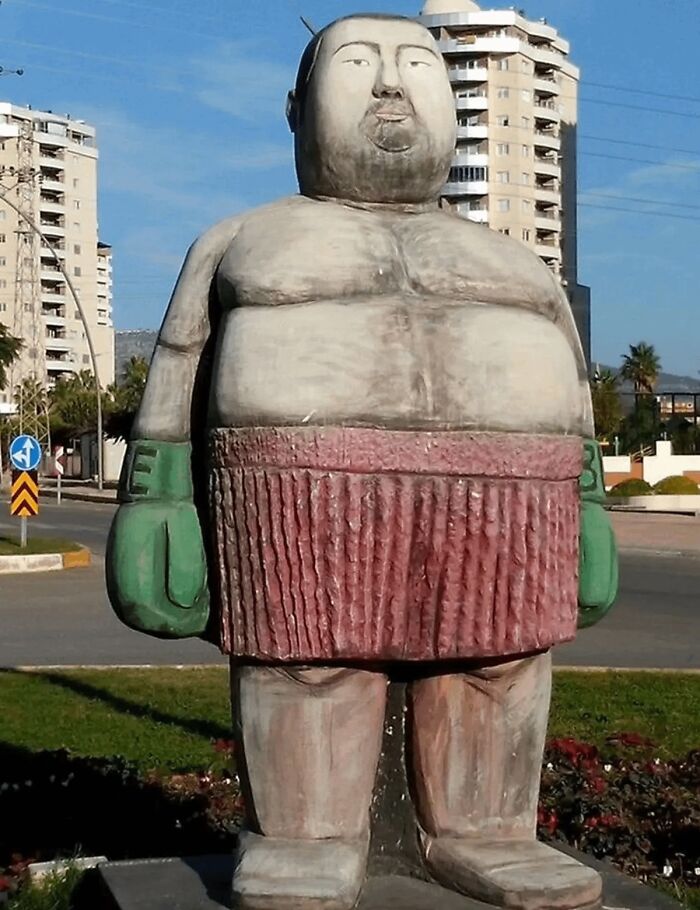A funny, oversized statue of a boxer standing outdoors as a bizarre example of public art.