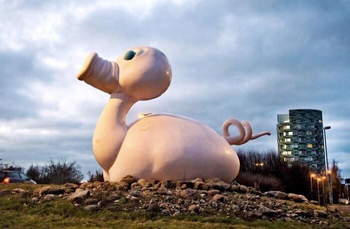 An odd pink animal sculpture at a roundabout, a unique example of public art.