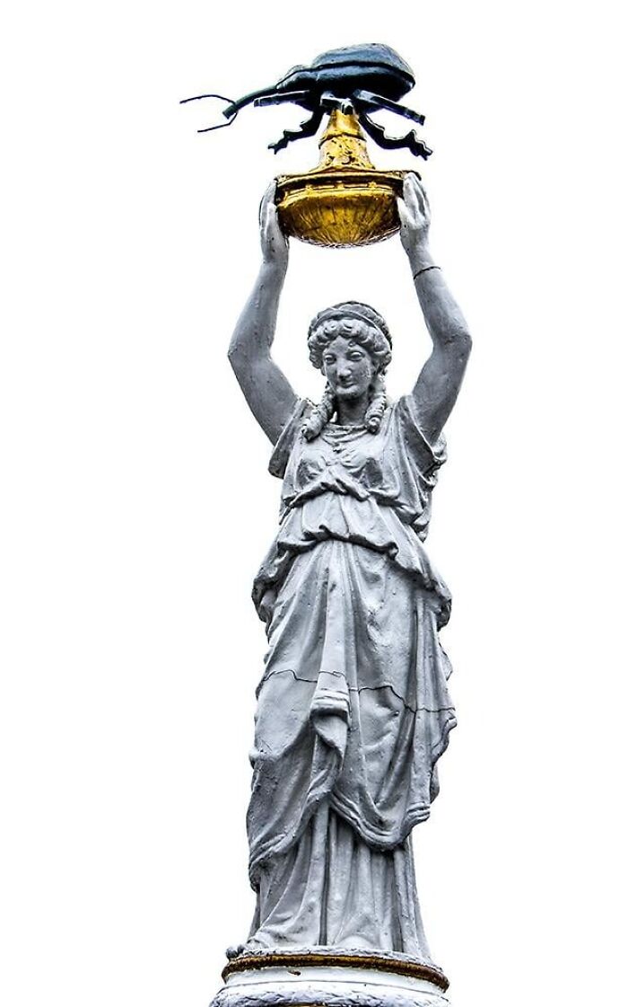 A stone statue of a woman holding a golden bowl with a beetle on top, a bizarre example of public art