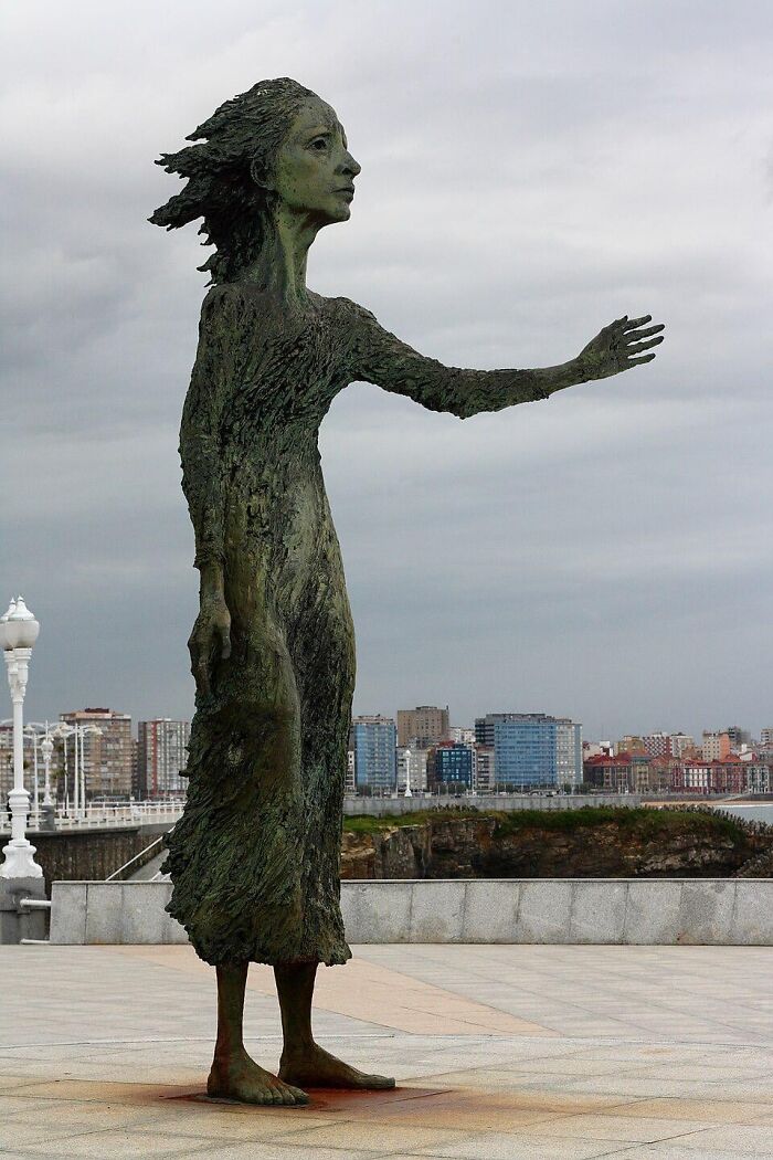 A bronze statue of a woman with her arm outstretched, representing examples of public art by the sea