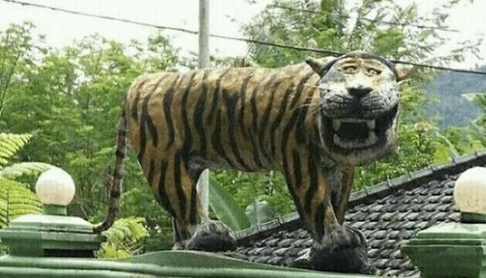 A funny and bizarre tiger statue with a wide derp smile standing on a roof, a hilarious public art piece