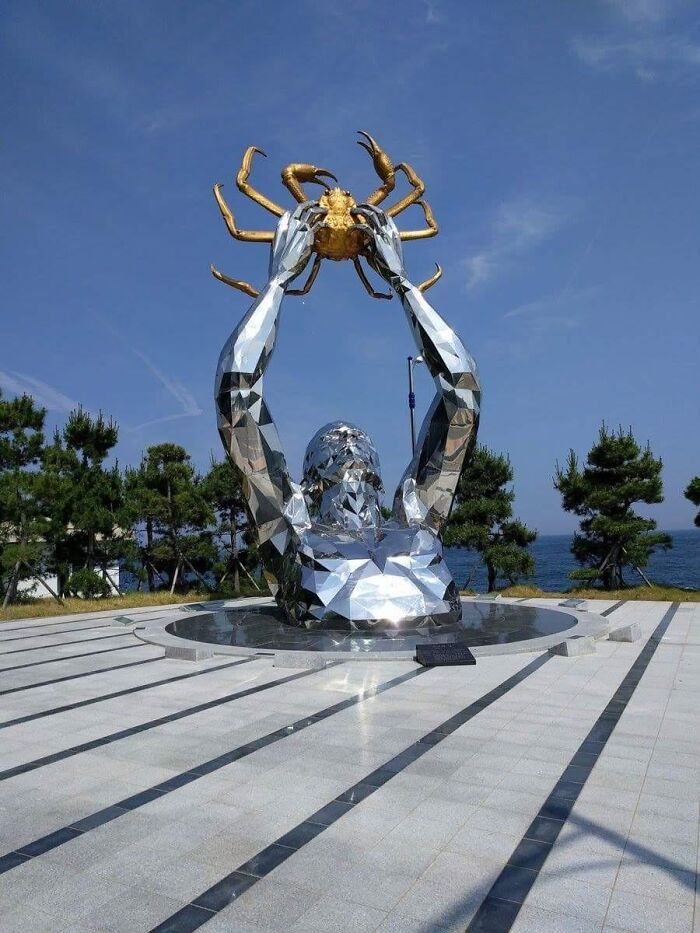 A metallic sculpture of a figure emerging from the ground holding a golden crab, as a piece of public art.