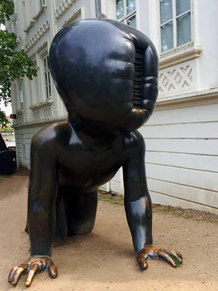 A dark bronze statue of a crawling baby with a bizarre slitted face, a piece of public art.