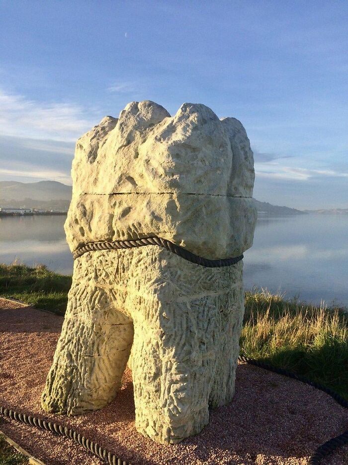 Large stone molar tooth sculpture positioned outdoors near water as a unique form of public art.
